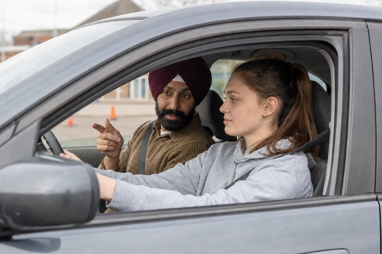 A learner driver with her hands on the wheel while her Akal instructor points ahead, guiding her through the lesson from the passenger seat